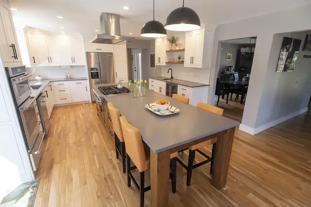 Stowe, VT kitchen with white cabinets, black dome pendants over a long wood dining table and oak floors