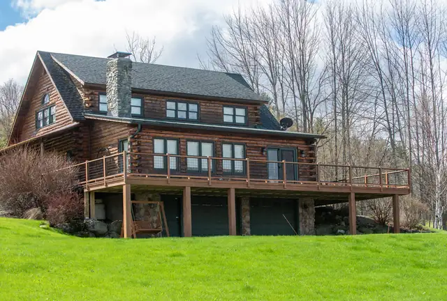 Wraparound deck with wood railings on a Vermont log home overlooking a green lawn