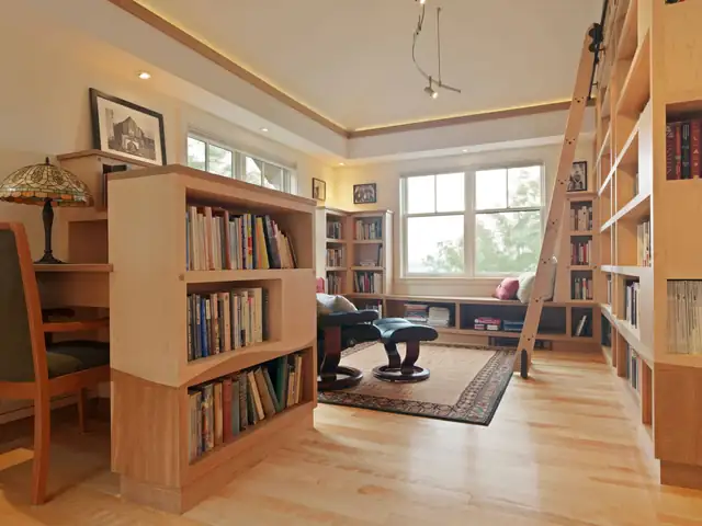 Custom built-in wood bookcases with a rolling library ladder, reading chair and window seat, made in Clar's Montpelier shop