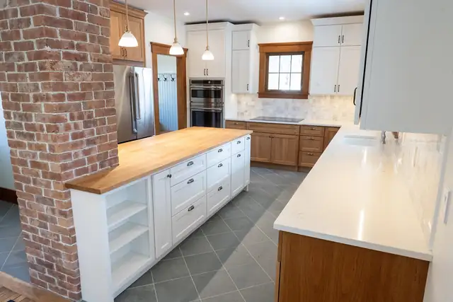 Kitchen remodel with exposed brick chimney column, white island with butcher block top and slate-look tile floor
