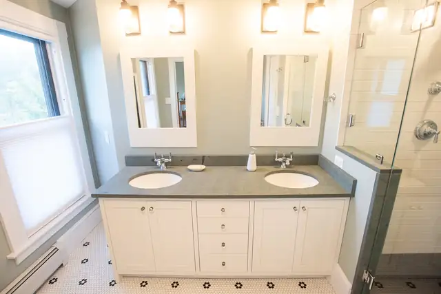 Bathroom remodel with white double vanity, dark stone top, framed mirrors and black-and-white tile floor