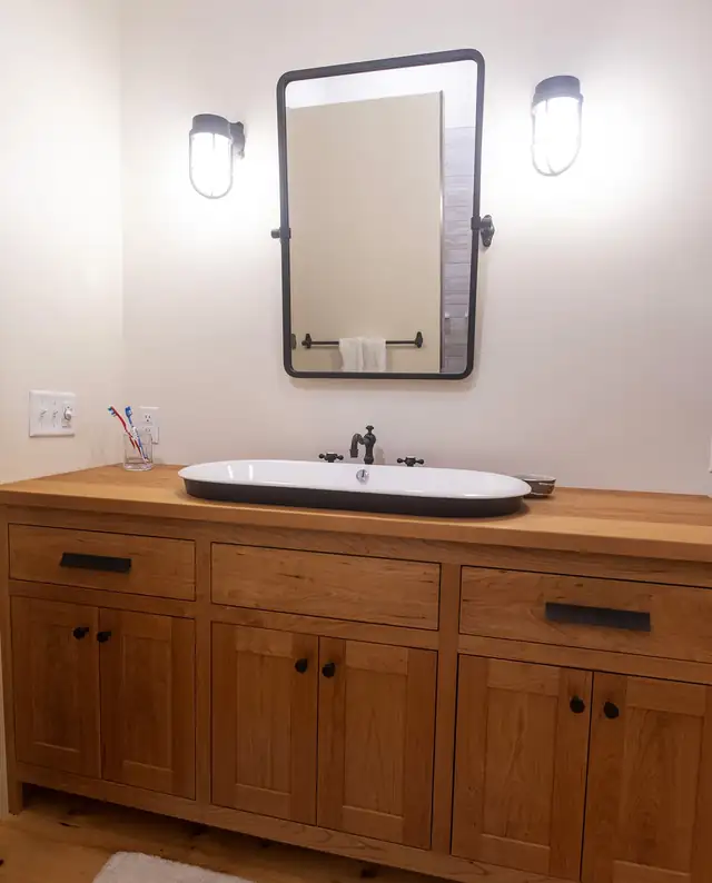 Bathroom with shop-built wood vanity, black vessel sink, black framed mirror and wall sconces