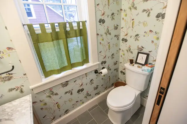 Powder room with botanical wallpaper, window cafe curtain and slate-look tile floor