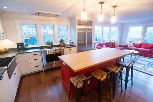 Kitchen remodel with red island and butcher block top, white cabinets, pendant lights and an open living room