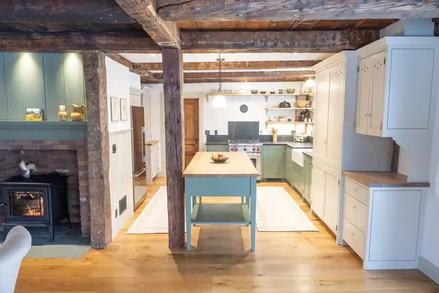 Vermont farmhouse kitchen remodel with exposed timber beams and posts, wood stove, sage cabinets and painted island